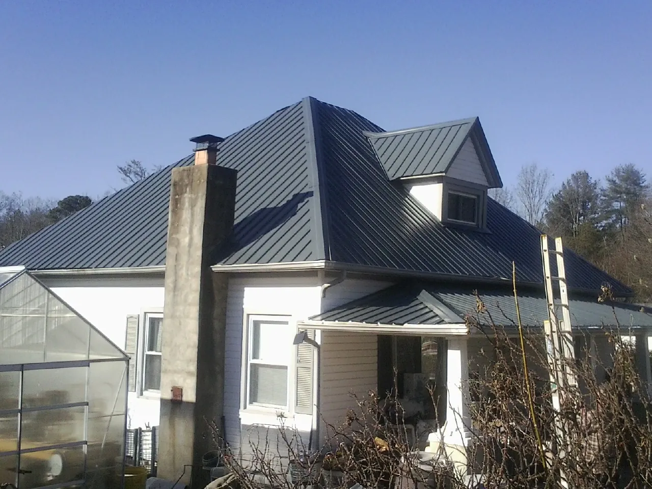 Dark blue standing seam metal roof on a white farmhouse with dormer — Slate & Tile Roof Repair by Roofing Brothers in Laramie