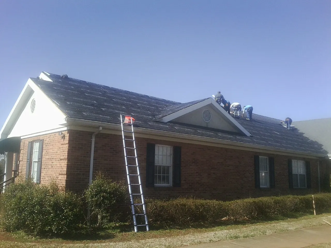 Crew tearing shingles off a brick ranch roof with a ladder set — Emergency Roof Repair work by our crew in Laramie