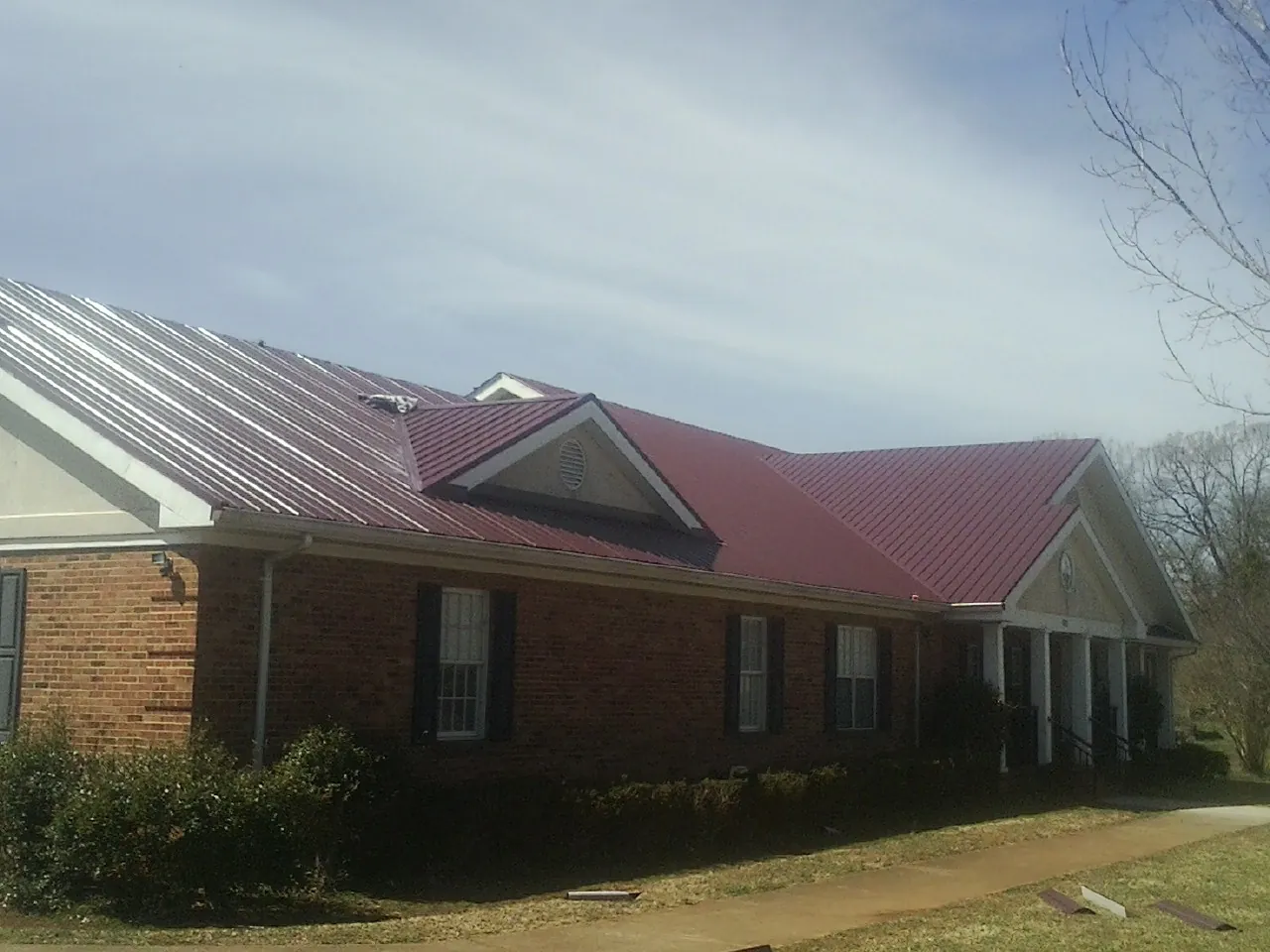 Red metal roof with gabled entries on a long brick building, from a Hail Damage Roof Repair job in Laramie