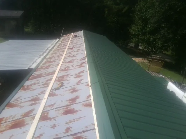 Old rusted panels beside newly installed green metal roofing — Wind Damage Roof Repair by Roofing Brothers in Laramie