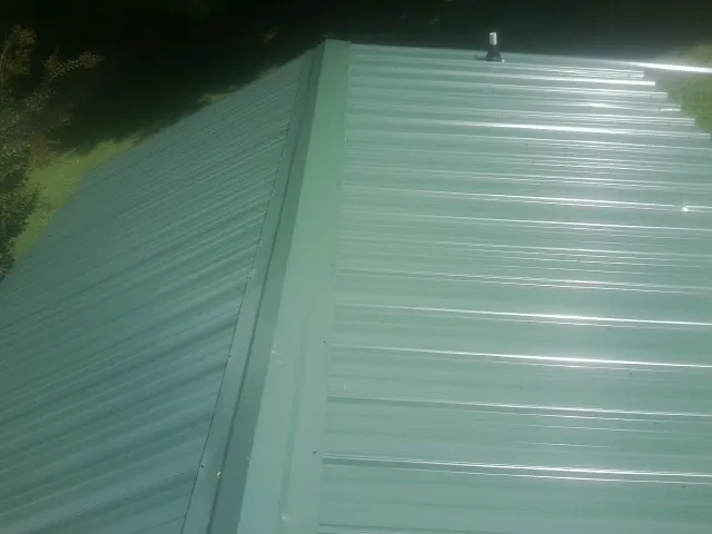 New green metal panels meeting at the ridge of a roof — Flat Roof Repair work by our crew in Laramie