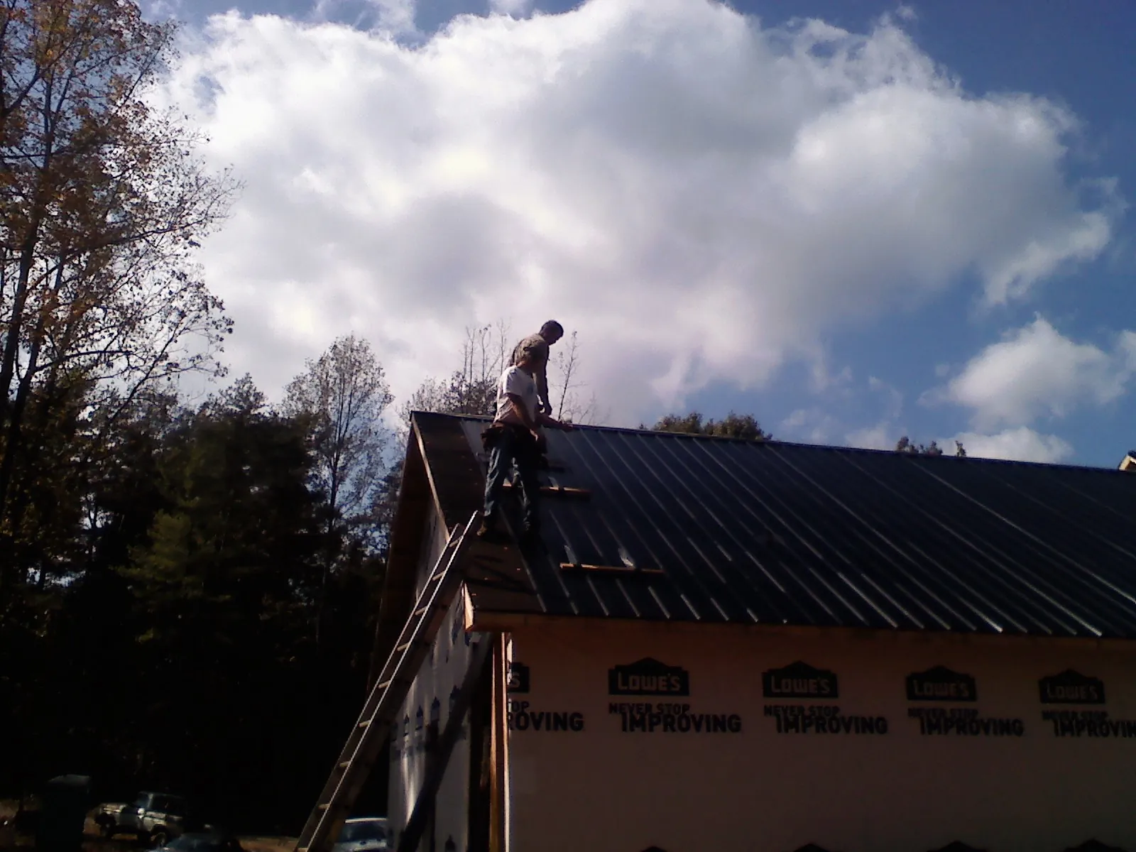 Roofer fastening dark metal panels high against a cloudy sky, from a Roof Inspection job in Laramie