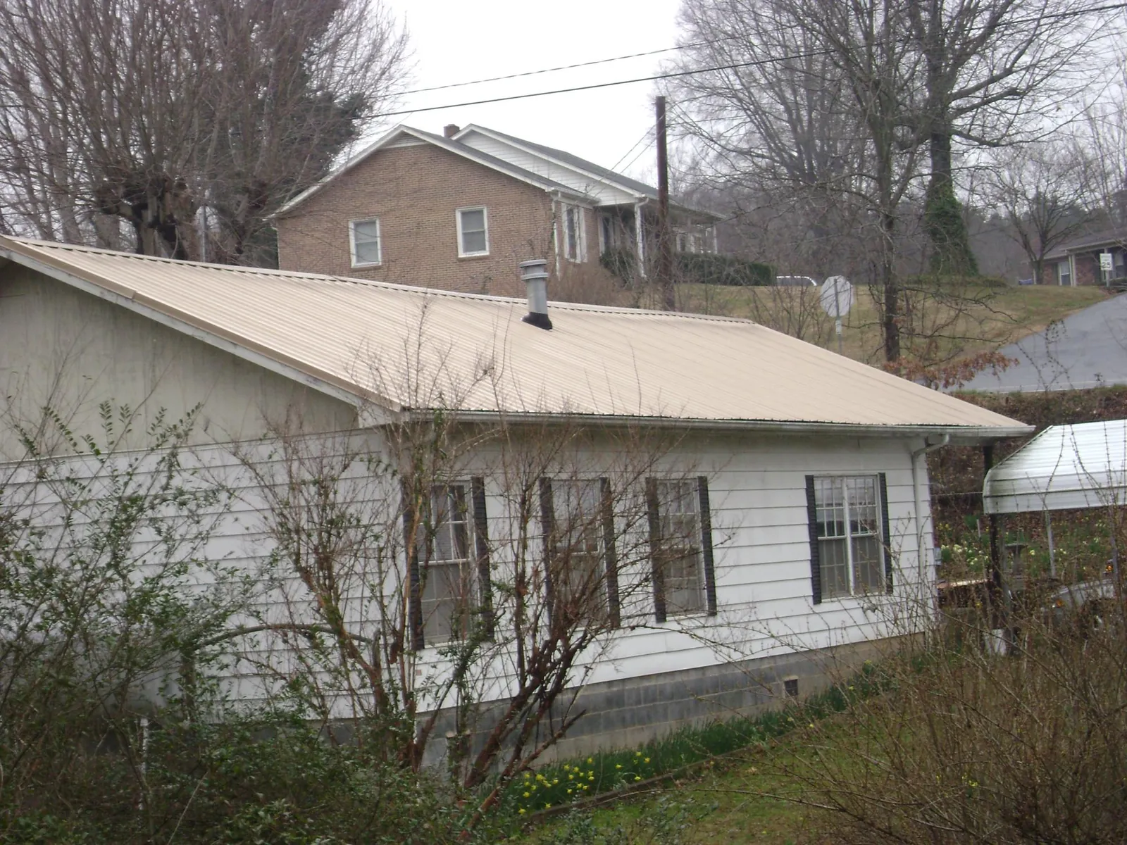 Tan metal roof on a white sided house set into a hillside — Commercial Roofing by Roofing Brothers in Laramie