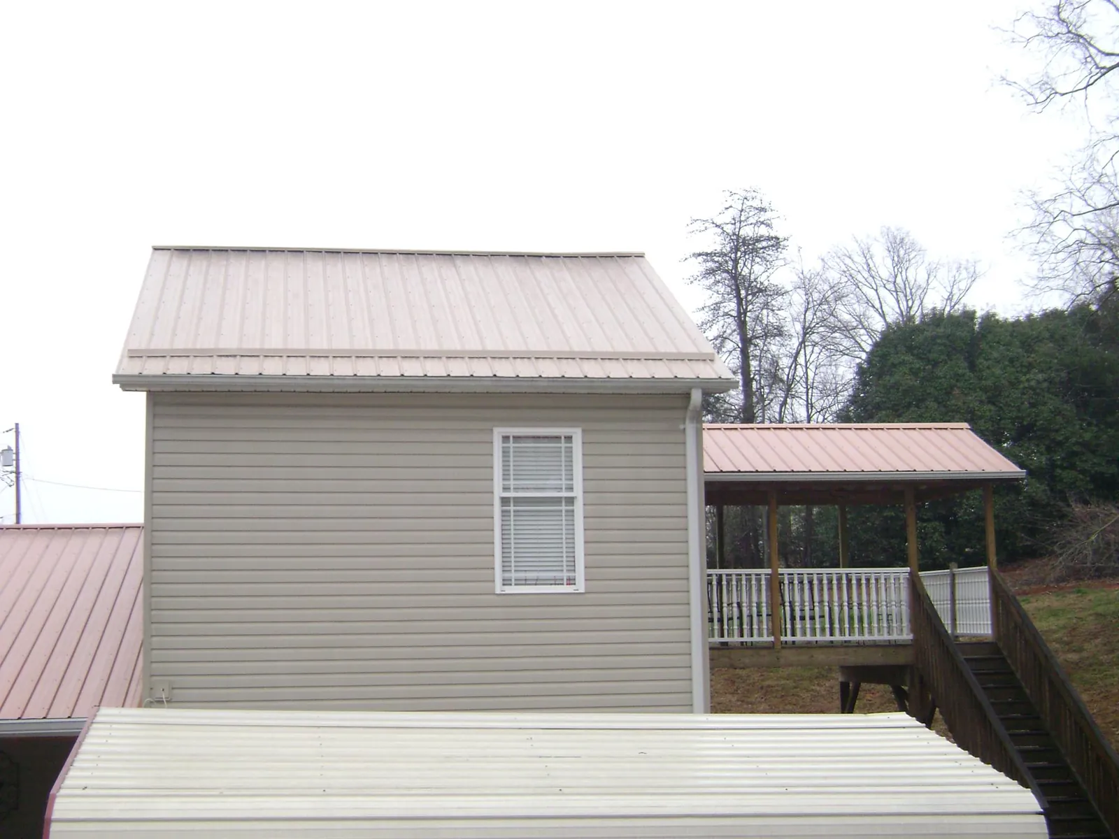 Tan metal roofs on a two story addition and attached porch, from a Roof Replacement job in Laramie